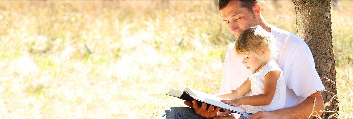 Father reading to his young daughter outdoors